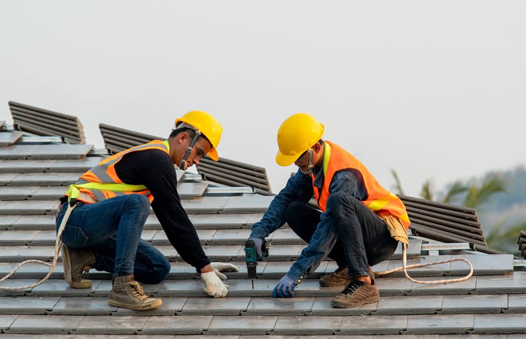 Construction workers installing roof tiles safely.